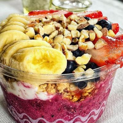 A vibrant acai bowl topped with sliced banana, strawberries, blueberries, granola, and chopped nuts.