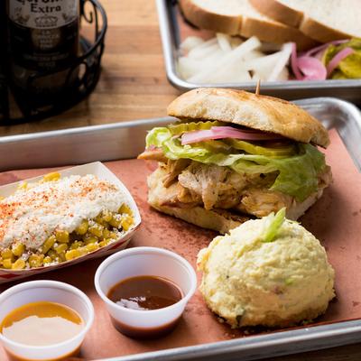 Plate with chicken sandwich, sauces, street corn and mashed potatoes