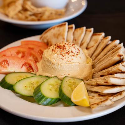 A plate of hummus garnished with paprika, surrounded by cucumber and tomato slices.