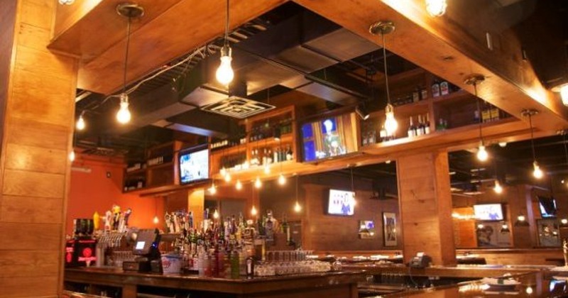 Warmly lit bar with wooden interior, multiple liquor bottles, and TVs mounted on the walls