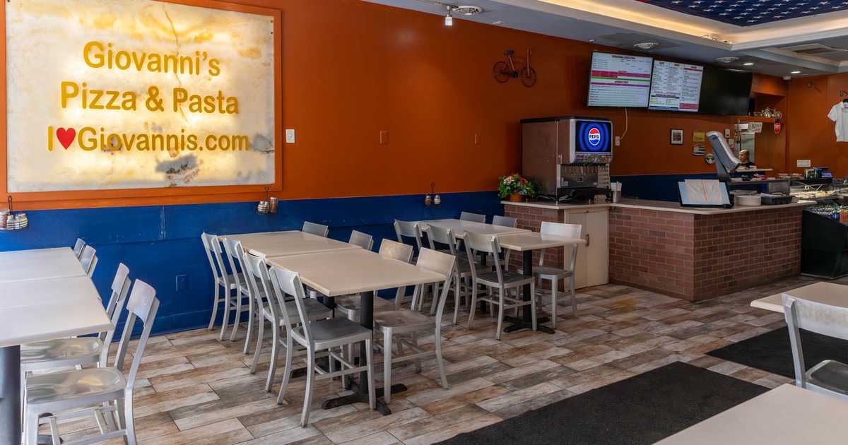 Interior with tables, chairs, a large sign and a counter area with menu screens.