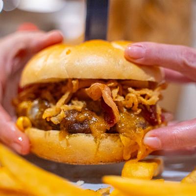 Hands holding a delicious looking bacon cheeseburger with fries on the side.