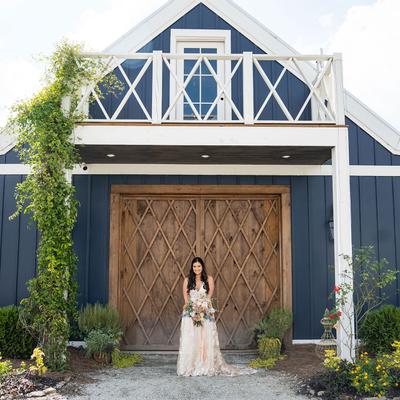 Bride holding a bouquet stands before a rustic, wooden barn door