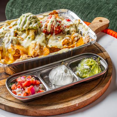 Loadeed nachos served with a side tray containing pico de gallo, sour cream and guacamole.