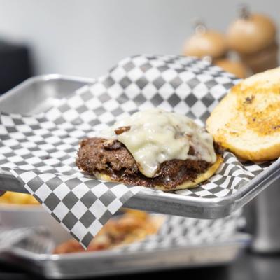 Person holding a tray with smash burger topped with melted cheese.