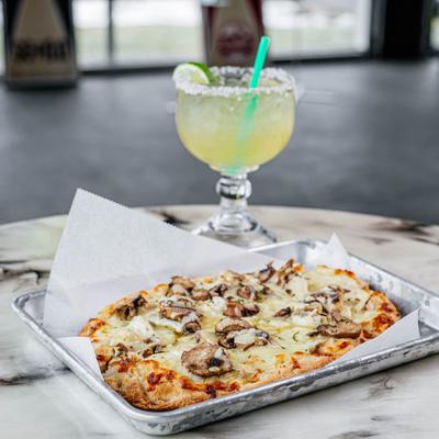 Mushroom pizza  on a metal tray, accompanied by a margarita cocktail.