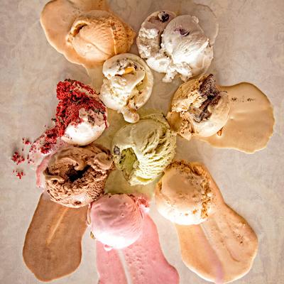 Melting scoops of various ice cream flavors form a colorful circle on a textured surface.