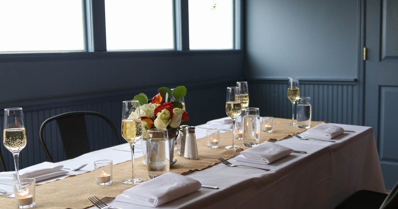 A table in a room with white table cloth, place settings, glasses of champagne and flowers