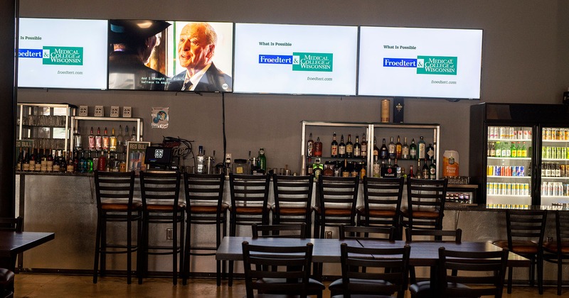 Interior, a bar with bar chairs, large wall TV screens, dining tables