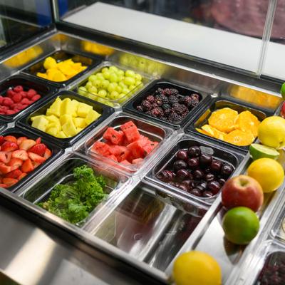 Refrigerated prep station featuring various fresh fruits in plastic and steel containers.