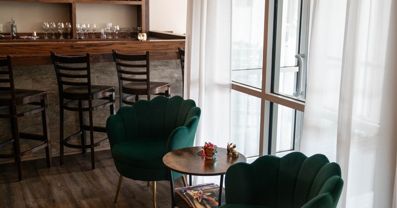 A cozy seating area with green armchairs and a small round table near a bar counter