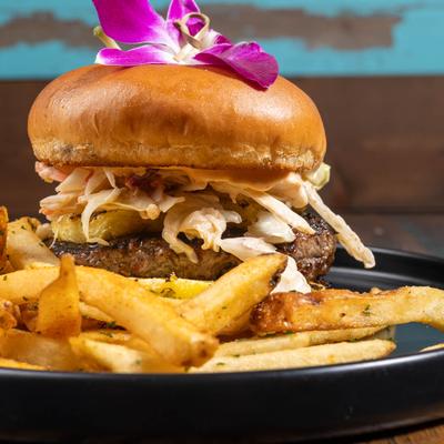 Burger with coleslaw, fries, and orchid garnish.