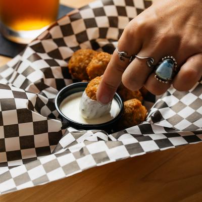 A hand dips street corn bite into a cup of house jalapeno ranch.