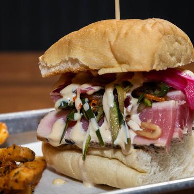 Seared tuna banh mi sandwich topped with slaw and pickled onions, served alongside fries.
