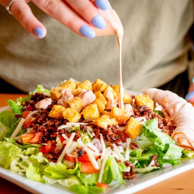A person drizzling sauce over a Caesar salad.