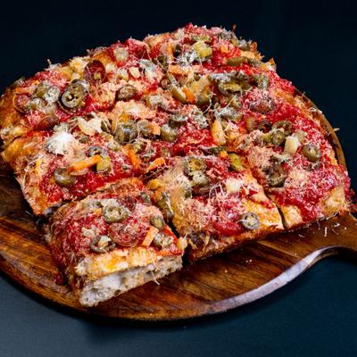 Spicy focaccia pizza slices on a wooden board with assorted toppings.