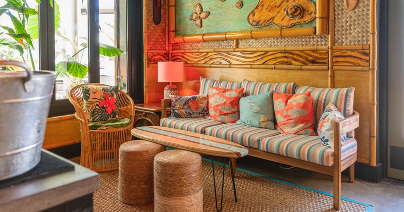 Interior, lounge area, sofa and wicker armchair, surfboard coffee table, tabourettes