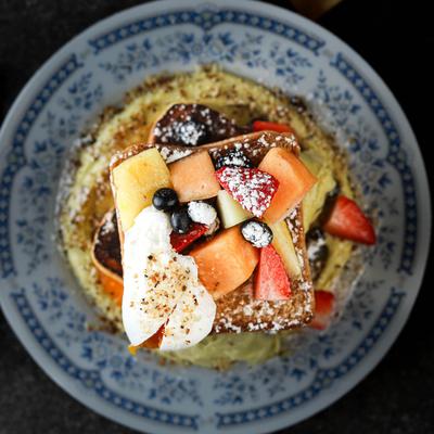 Pancakes topped with fresh mixed fruit, whipped cream, and powdered sugar.