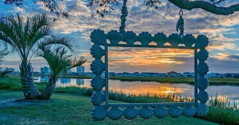 Sunset over a calm river framed by a decorative seashell-bordered frame