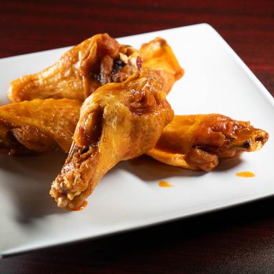 A plate with five hot wings sits on a wooden table.