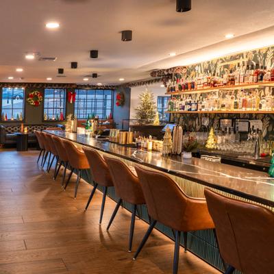 Elegant bar with a long counter, leather stools, and Christmas decorations.