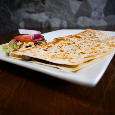 Large quesadilla served with a small salad on a square plate.