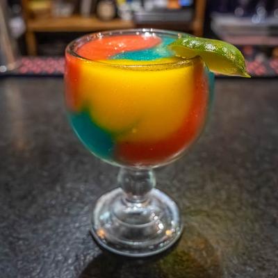 Colorful layered cocktail with lime garnish.