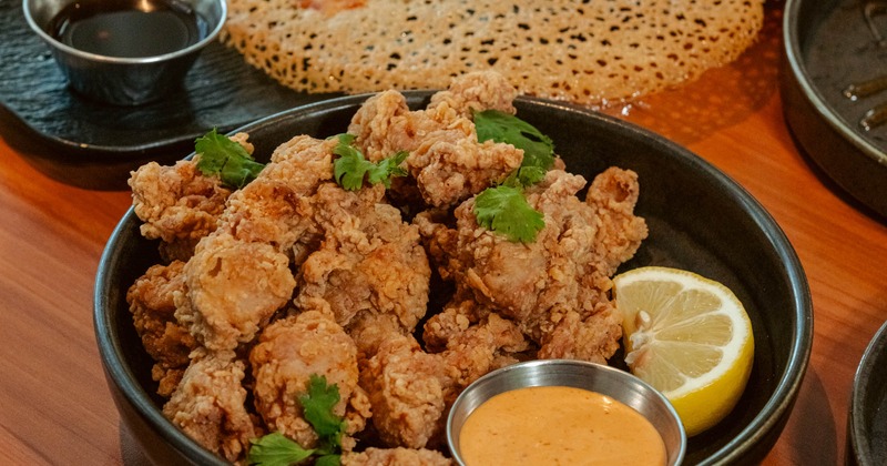 Bowl of fried chicken bites with dipping sauces and a lemon slice