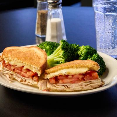 Turkey Melt sandwich served with broccoli on the side and a drink.