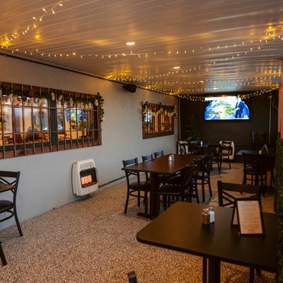 Patio area with wooden dining table, black chairs and overhead string lights.