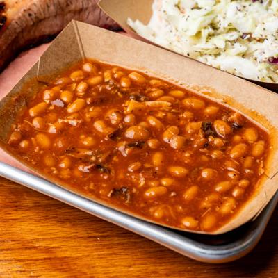 Barbecue tray featuring baked beans, creamy coleslaw, sliced brisket, and sausage.