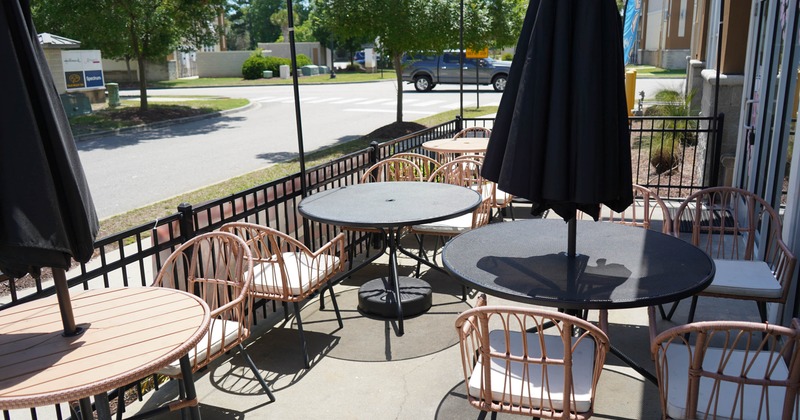 Outdoor seating area, tables, wicker chairs with cushions and a large umbrella