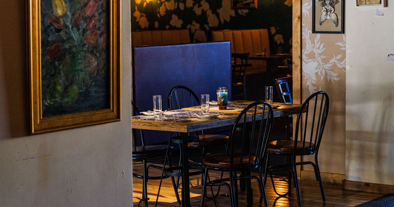 Interior with wooden table set for dining, black metal chairs and art pictures on the walls.