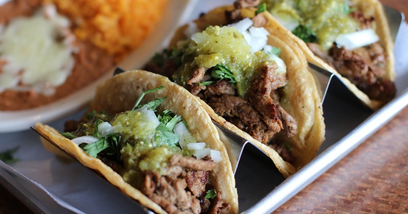 Bistec tacos topped with cilantro, onions and roasted tomatillo sauce