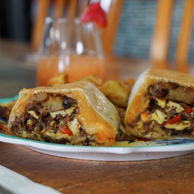 A close-up of a smoked brisket sandwich with scrambled eggs, cheese, and smashed potatoes.