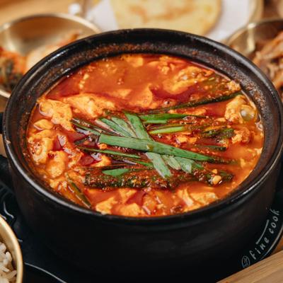 Spicy soft tofu stew served in a traditional earthenware pot, close-up.