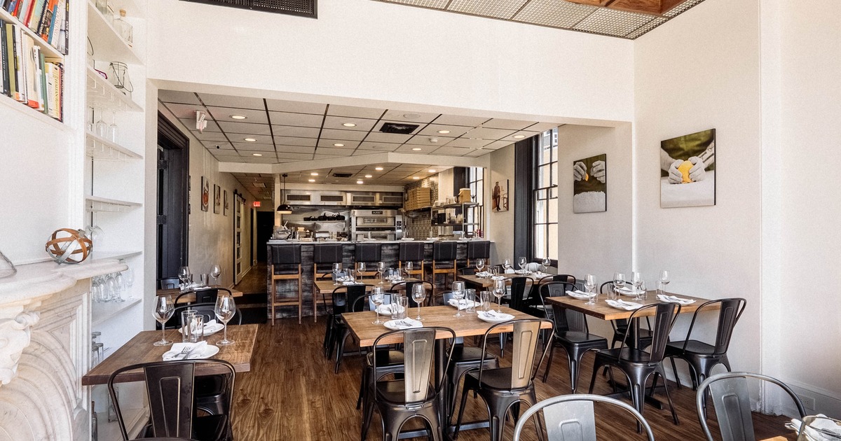 A modern interior - wooden tables, chairs, an open kitchen and abstract artwork on white walls