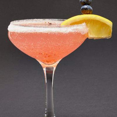 Pink cocktail drink, garnished with blueberries and orange, close up.