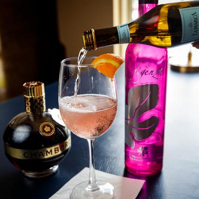 Sparkling wine is poured into a glass with a pink drink, on a table with liqueur and fig vodka.