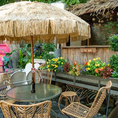 Outdoor seating features a Tiki-style thatched umbrella, a glass-top table and chairs.