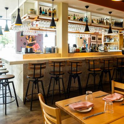 Bar area with wooden stools, well-stocked shelves, and hanging glasses.