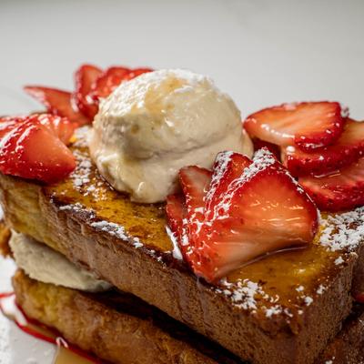 French toast stuffed with cheesecake cream and topped with strawberries and strawberry syrup.