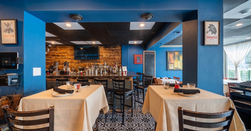 A restaurant interior with tables, a bar, and blue walls.