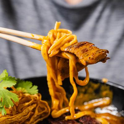 Chopsticks lifting curry noodles with a piece of grilled meat.