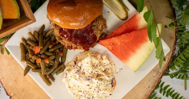 Pulled pork sandwich served with green beans, coleslaw, pickle, and watermelon
