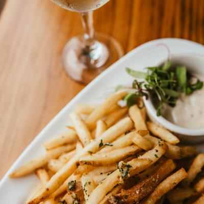 Seasoned fries served with a dipping sauce and a glass of white wine, close-up.