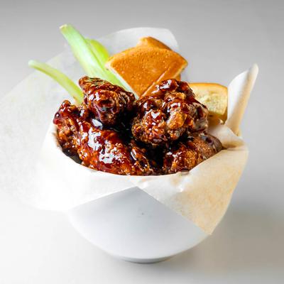 A bowl of teriyaki BBQ chicken wings with celery sticks and cornbread.