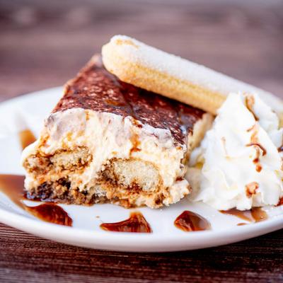 A plate of tiramisu with whipped cream and a ladyfinger.