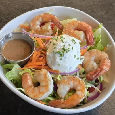 A fresh salad topped with grilled shrimp, shredded carrots, and a dollop of herb goat cheese.