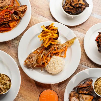 Fried whole fish with rice, fries, and vegetables surrounded by plates of food.